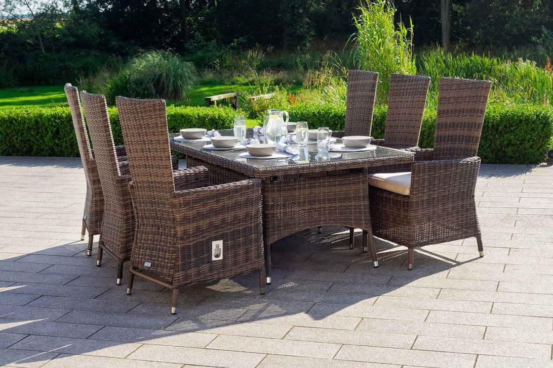 Bruine wicker eethoek met glazen tafelblad op een stenen terras.