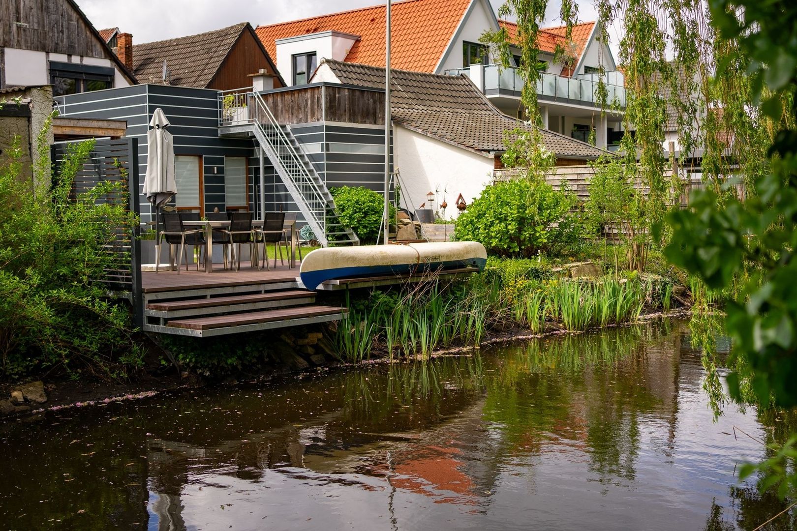 Woning met terras en kano naast een begroeide tuinvijver